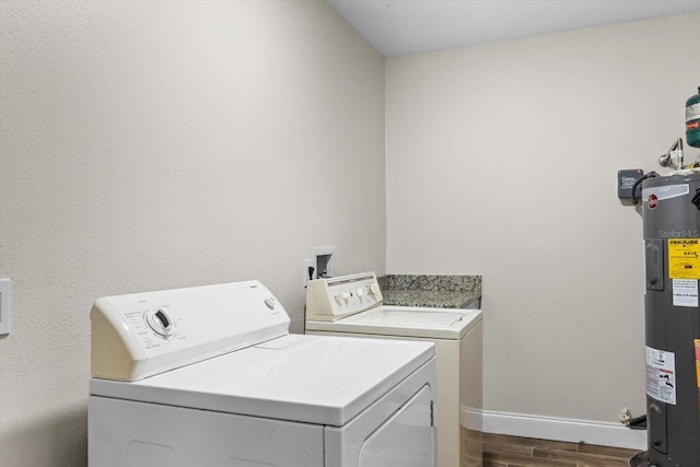 laundry area featuring electric water heater, laundry area, baseboards, washer and dryer, and dark wood finished floors