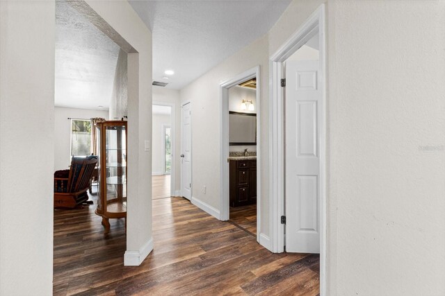 corridor featuring baseboards, visible vents, dark wood finished floors, and a sink