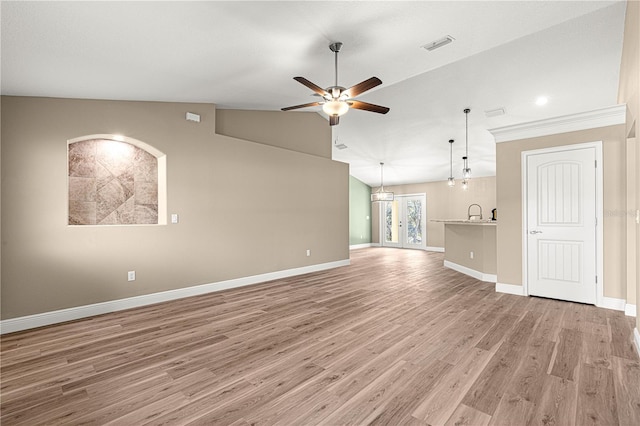 unfurnished living room featuring ceiling fan with notable chandelier, wood finished floors, visible vents, baseboards, and vaulted ceiling