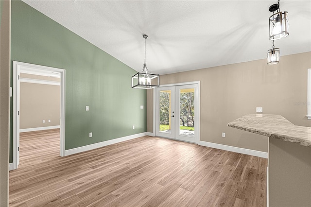 unfurnished dining area featuring french doors, vaulted ceiling, baseboards, and wood finished floors