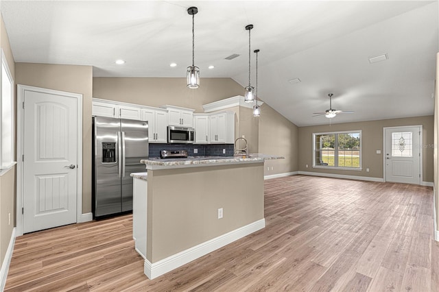 kitchen featuring stainless steel appliances, white cabinets, open floor plan, hanging light fixtures, and light stone countertops