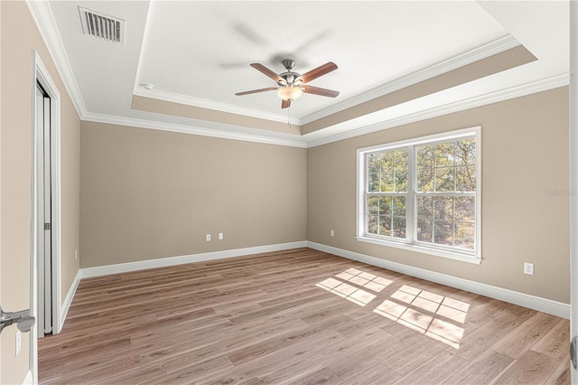 spare room featuring a tray ceiling, crown molding, visible vents, light wood-style floors, and baseboards