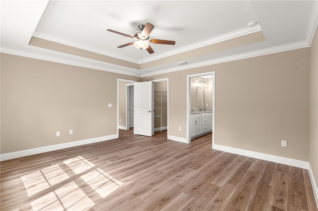 unfurnished bedroom with a tray ceiling, a closet, light wood-type flooring, and baseboards