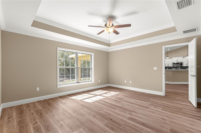 unfurnished room with visible vents, a tray ceiling, and light wood-style flooring