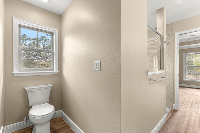 bathroom with baseboards, a tile shower, toilet, and wood finished floors