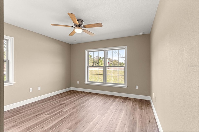 spare room featuring light wood finished floors, a ceiling fan, and baseboards