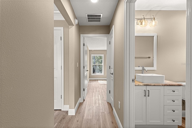 corridor with baseboards, visible vents, a textured wall, light wood-type flooring, and a sink