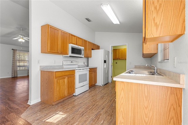 kitchen featuring white appliances, a sink, light wood-style floors, vaulted ceiling, and light countertops