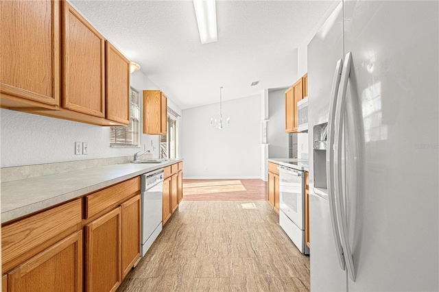 kitchen featuring white appliances, a sink, light countertops, hanging light fixtures, and an inviting chandelier