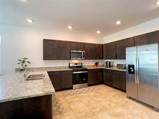 kitchen featuring a peninsula, a sink, dark brown cabinets, appliances with stainless steel finishes, and light stone countertops