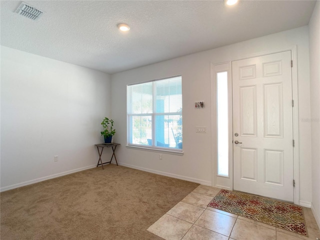 foyer with light tile patterned floors, baseboards, visible vents, light colored carpet, and a textured ceiling