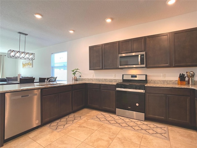 kitchen featuring light stone counters, dark brown cabinetry, a sink, appliances with stainless steel finishes, and pendant lighting