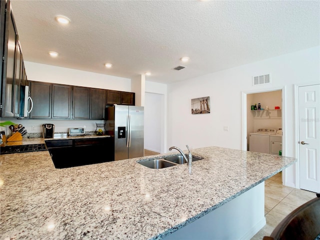 kitchen featuring stainless steel appliances, a sink, visible vents, washer and dryer, and dark brown cabinets