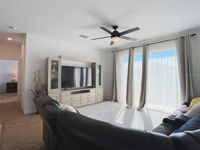 living room with light carpet, a ceiling fan, visible vents, and a textured ceiling