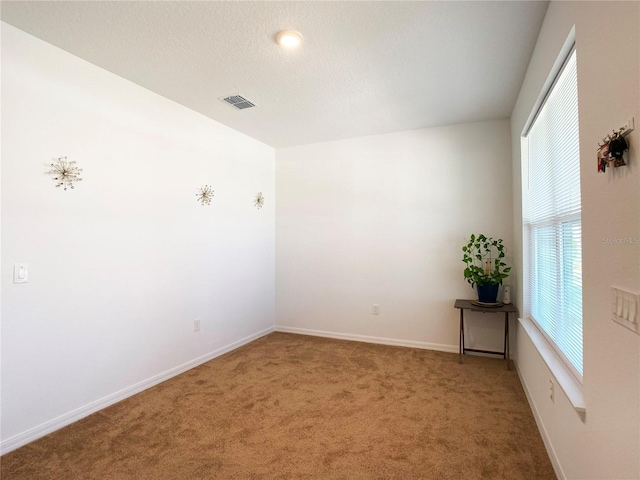 carpeted spare room featuring baseboards, visible vents, and a textured ceiling