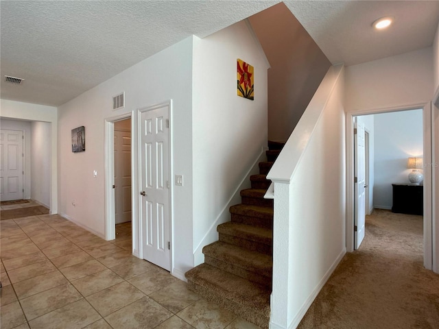 staircase with a textured ceiling, visible vents, and tile patterned floors