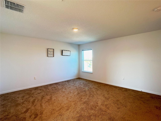 spare room with visible vents, dark carpet, a textured ceiling, and baseboards