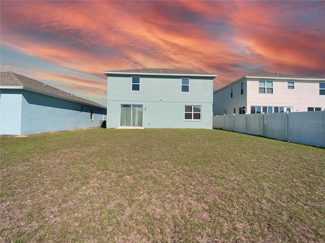 back of property at dusk featuring a yard, fence, and stucco siding