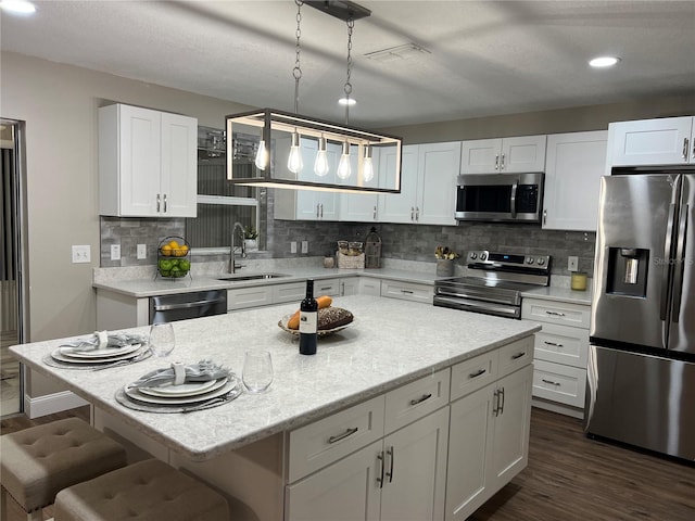 kitchen featuring a kitchen island, appliances with stainless steel finishes, decorative light fixtures, white cabinetry, and a sink