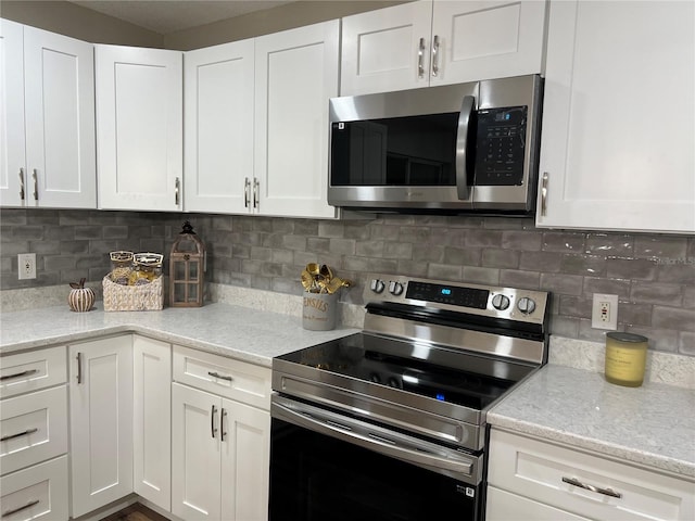 kitchen with stainless steel appliances, light stone countertops, white cabinetry, and tasteful backsplash