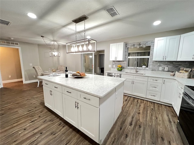 kitchen with visible vents, white cabinets, a center island, hanging light fixtures, and a sink