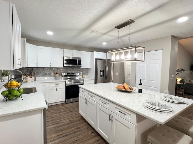 kitchen featuring white cabinets, appliances with stainless steel finishes, a center island, hanging light fixtures, and light stone countertops