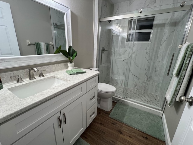 bathroom with toilet, vanity, a marble finish shower, and wood finished floors