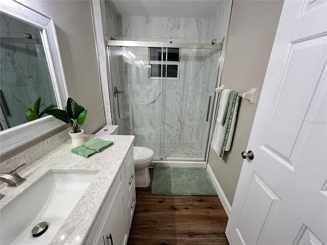 bathroom featuring a marble finish shower, baseboards, toilet, wood finished floors, and vanity