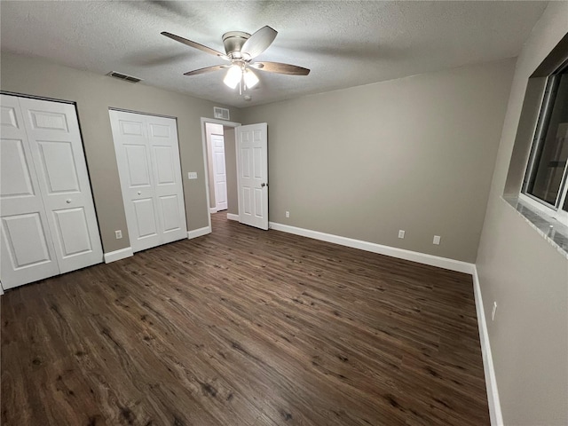 unfurnished bedroom featuring multiple closets, visible vents, baseboards, and dark wood-style floors