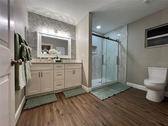 bathroom featuring double vanity, a marble finish shower, wood finished floors, a textured ceiling, and a sink