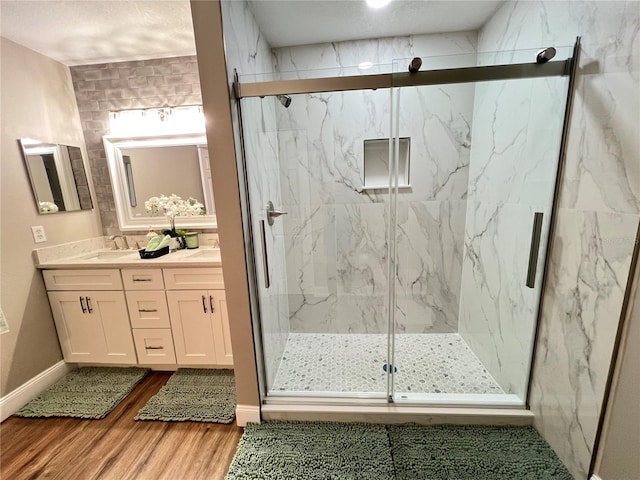 full bathroom with a marble finish shower, double vanity, a sink, wood finished floors, and baseboards