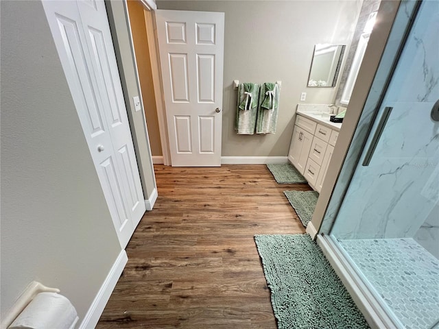 bathroom with a marble finish shower, baseboards, wood finished floors, and vanity