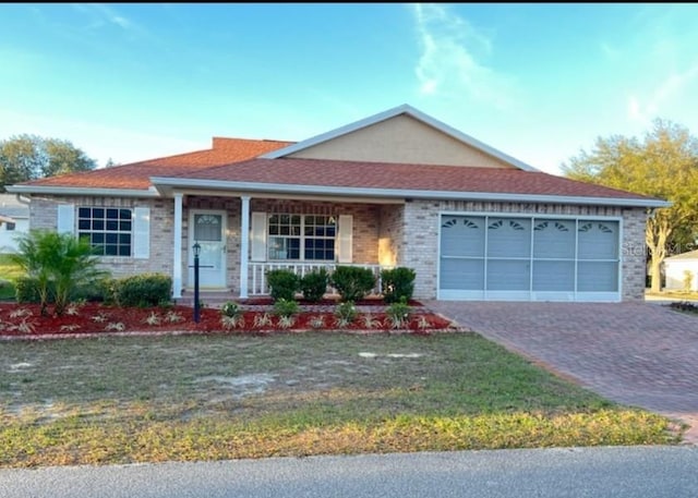 ranch-style house with brick siding, a front yard, covered porch, decorative driveway, and an attached garage