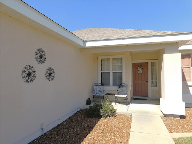 view of exterior entry featuring a porch, roof with shingles, and stucco siding