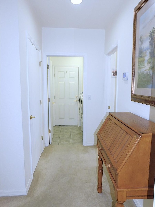 hall featuring light carpet, baseboards, and separate washer and dryer