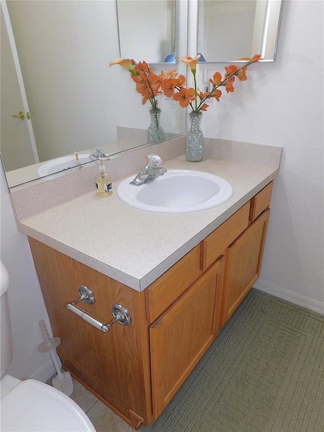 half bath with baseboards, vanity, and toilet