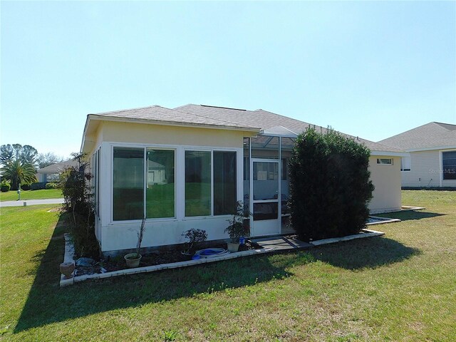 back of house featuring a shingled roof, a lawn, a lanai, and stucco siding