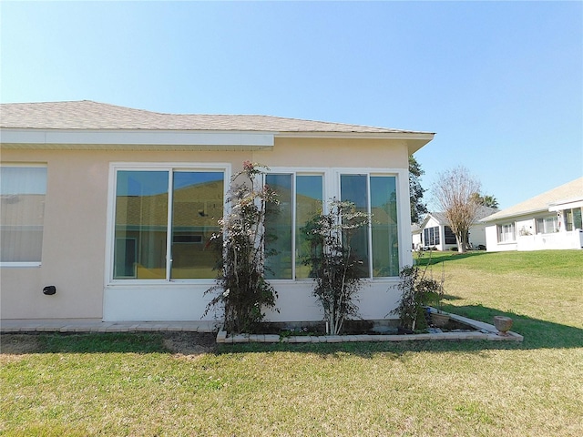 view of home's exterior with a yard, roof with shingles, and stucco siding