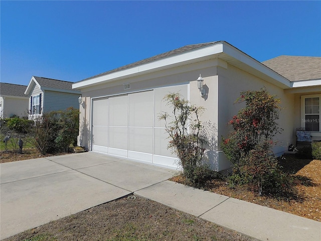 view of side of home featuring concrete driveway, roof with shingles, and stucco siding