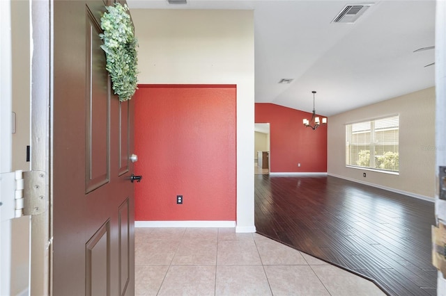 foyer entrance featuring lofted ceiling, light tile patterned floors, visible vents, and an inviting chandelier