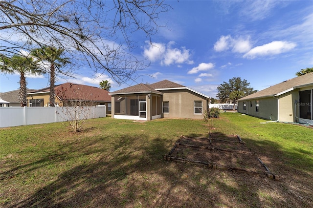 rear view of house featuring a lawn, fence private yard, a sunroom, and stucco siding