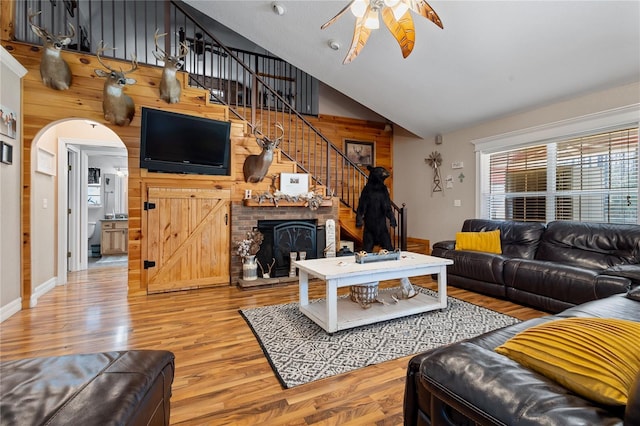 living area with arched walkways, stairway, a ceiling fan, wood finished floors, and high vaulted ceiling