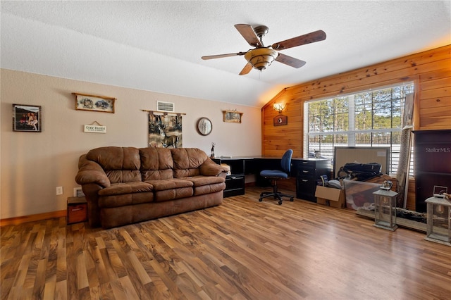 living room featuring lofted ceiling, visible vents, wood walls, a textured ceiling, and wood finished floors