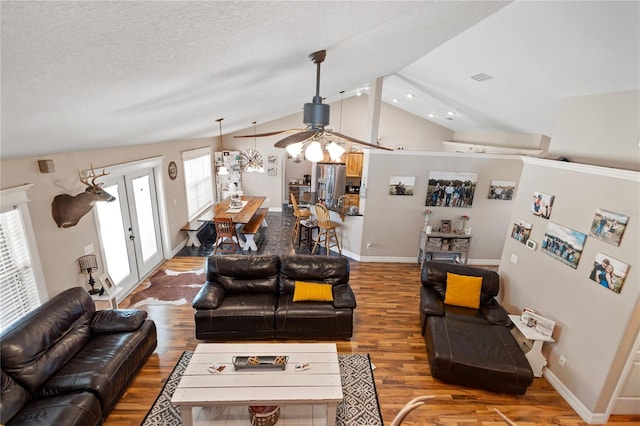 living area featuring lofted ceiling, visible vents, a textured ceiling, wood finished floors, and baseboards