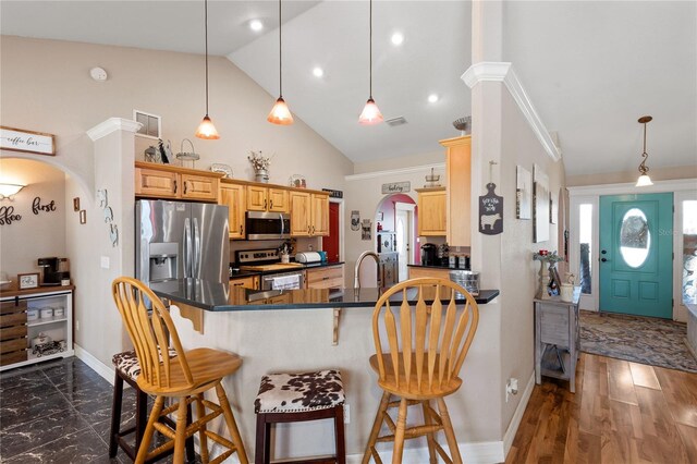 kitchen featuring arched walkways, a peninsula, appliances with stainless steel finishes, dark countertops, and a kitchen bar