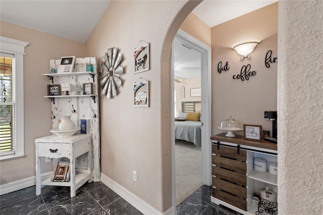 corridor featuring arched walkways, marble finish floor, lofted ceiling, and baseboards