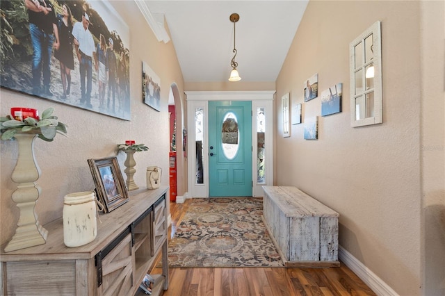 foyer entrance featuring arched walkways, a textured wall, lofted ceiling, wood finished floors, and baseboards