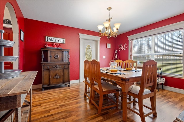 dining room featuring a chandelier, arched walkways, wood finished floors, and baseboards