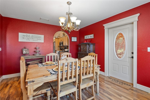 dining space featuring arched walkways, visible vents, an inviting chandelier, and wood finished floors