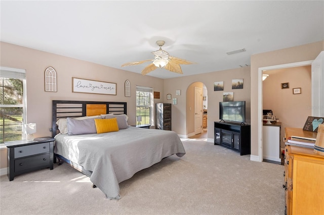 bedroom with arched walkways, light carpet, visible vents, and baseboards